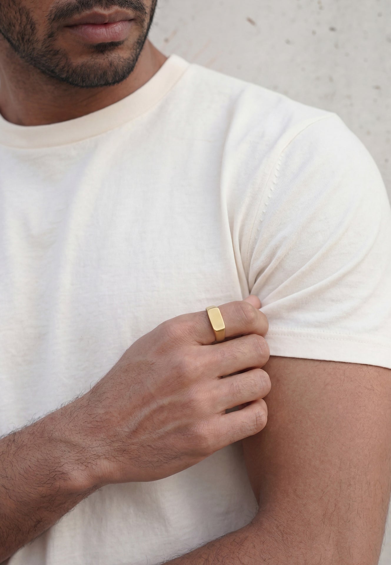 Man wearing a white t-shirt and gold ring on his finger, holding his arm.
