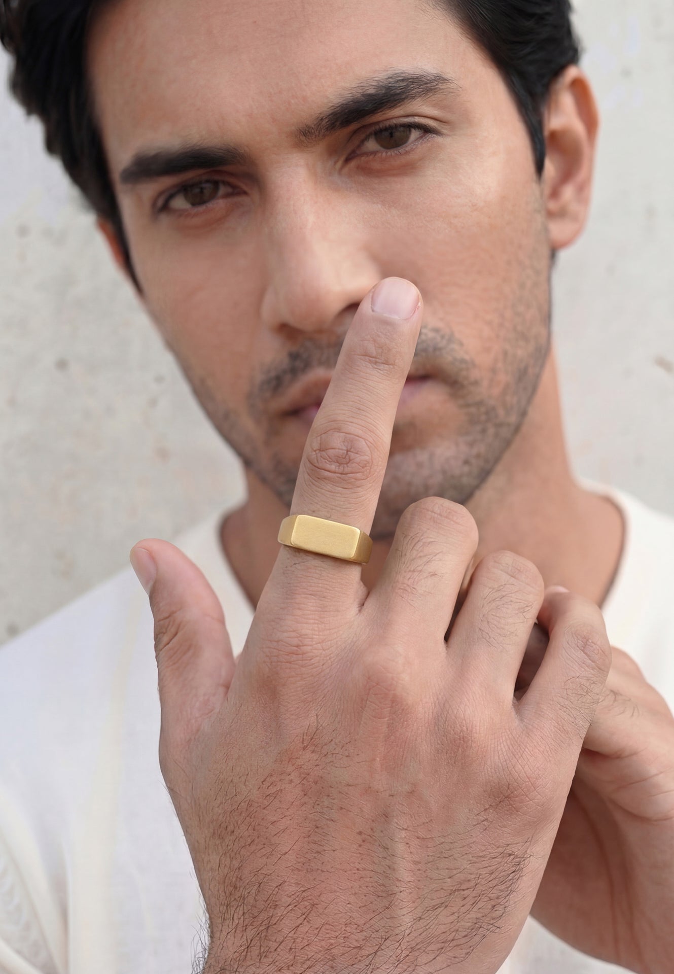 Man wearing a gold ring on his finger against a neutral background
