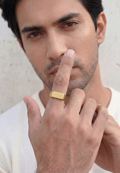 Man wearing a gold ring on his finger against a neutral background