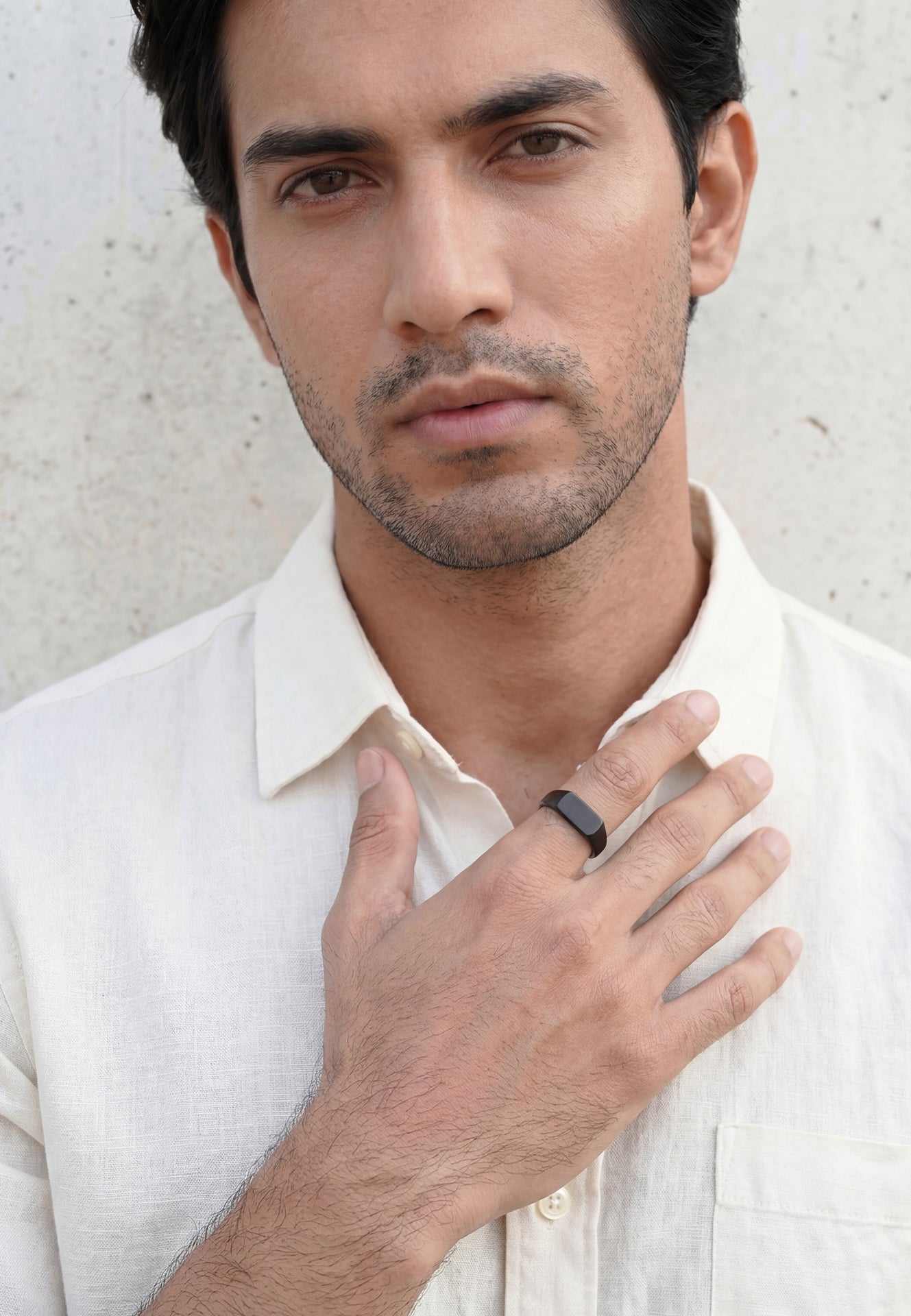 Man wearing a white shirt with a black ring on his finger against a light background