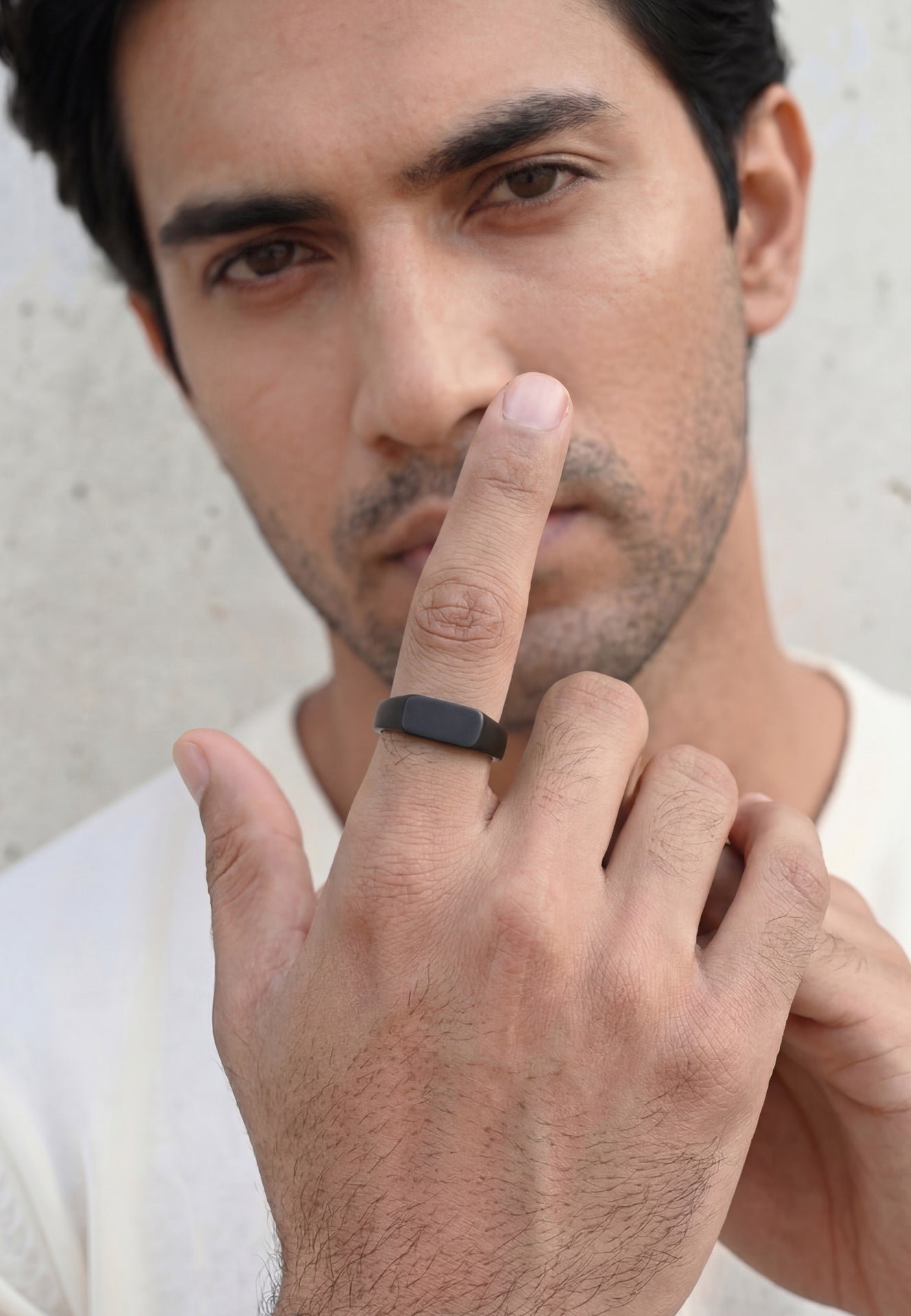 Man wearing a black ring on his finger against a neutral background