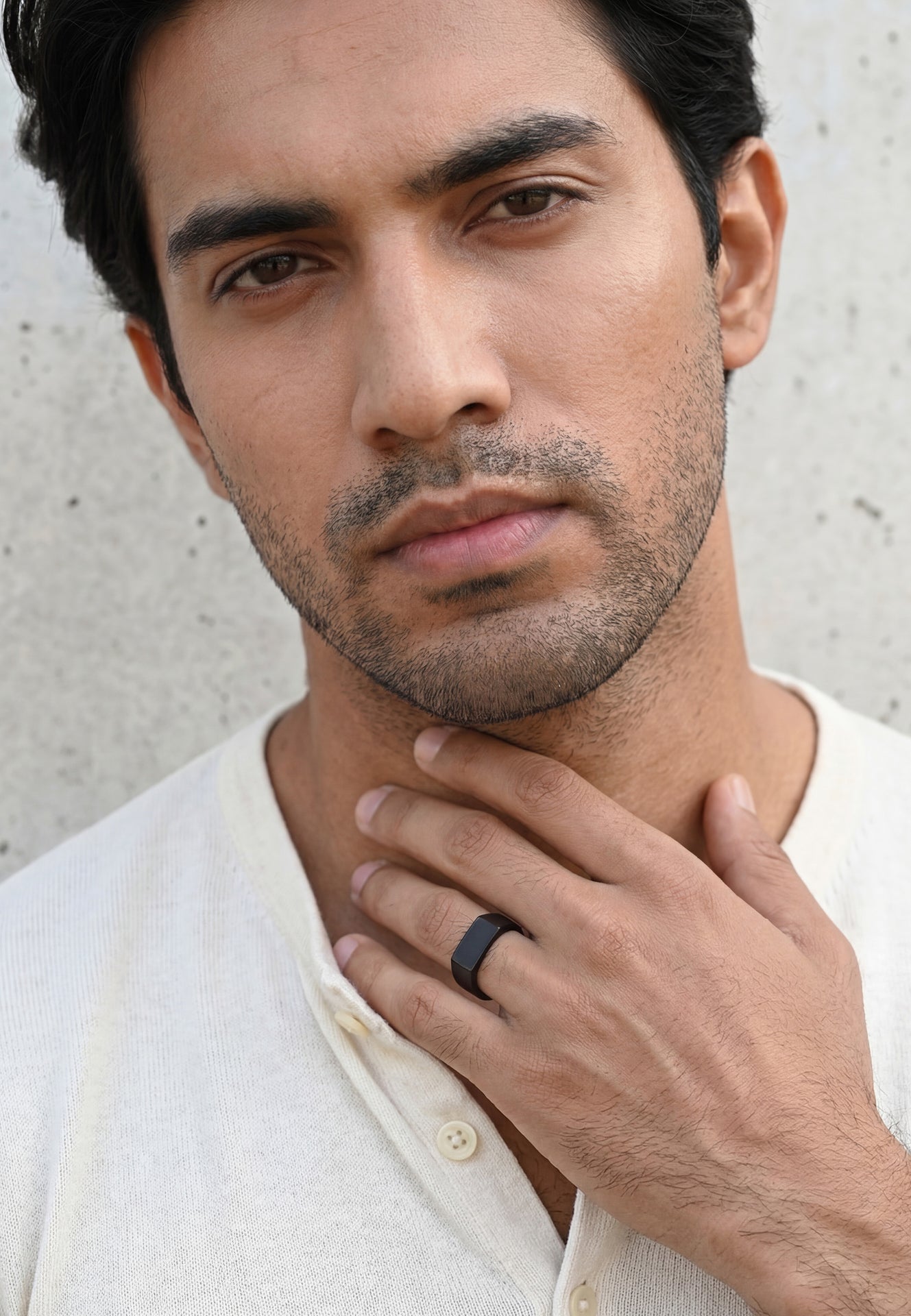 Man wearing a white shirt with a black ring on his finger against a neutral background