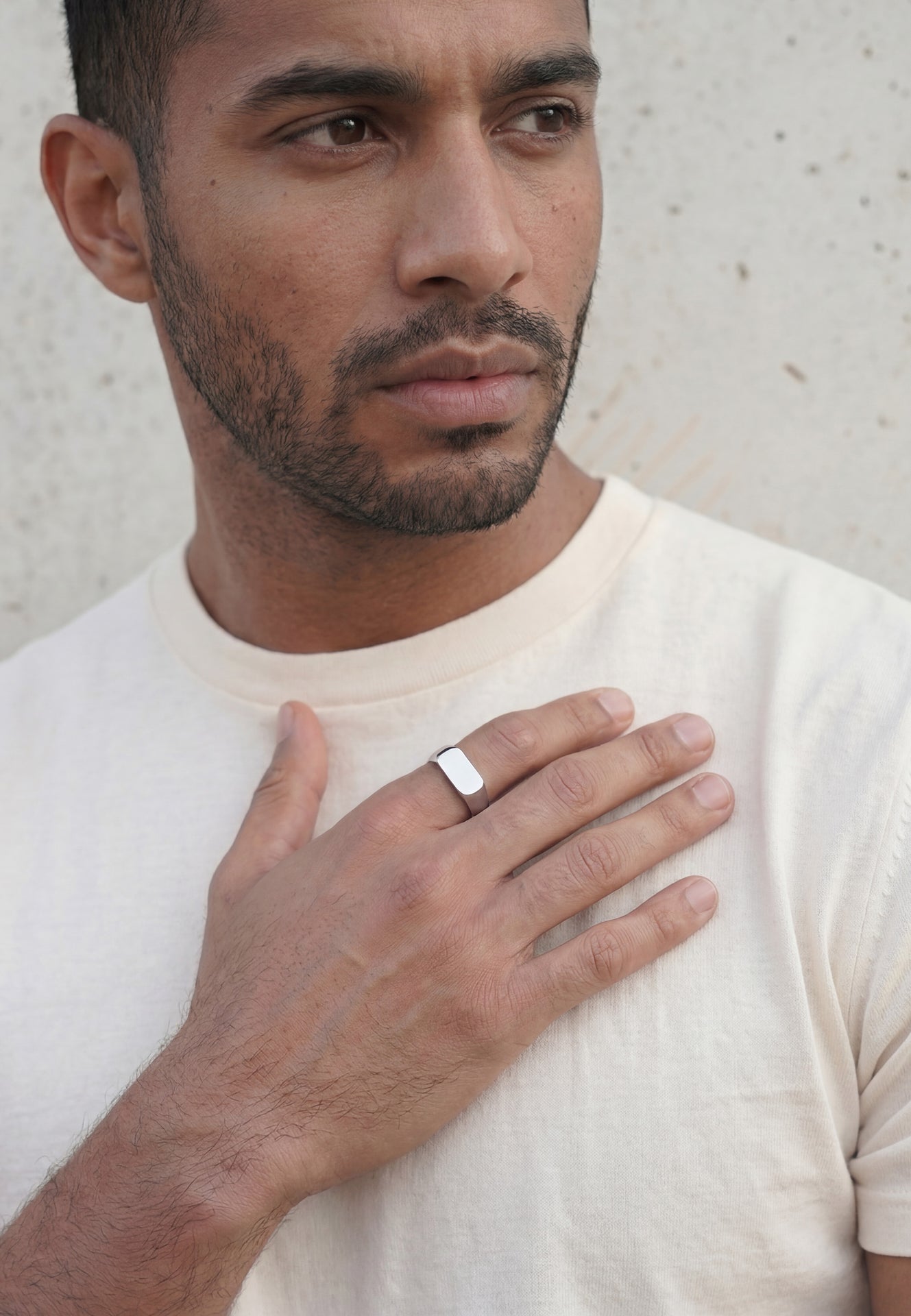 Man wearing a white shirt with a ring on his finger against a light background