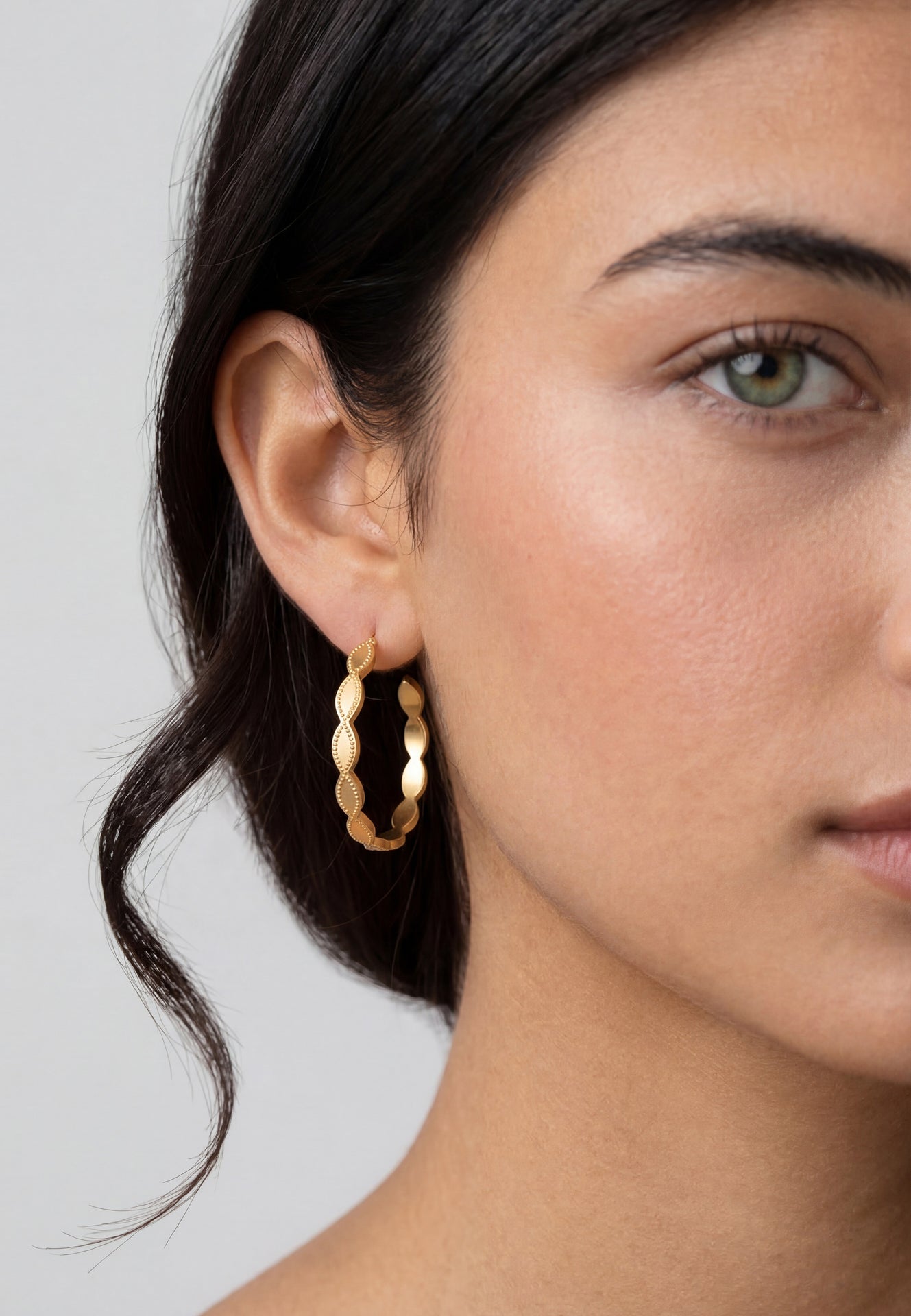Close-up of a woman wearing gold hoop earrings with a neutral background