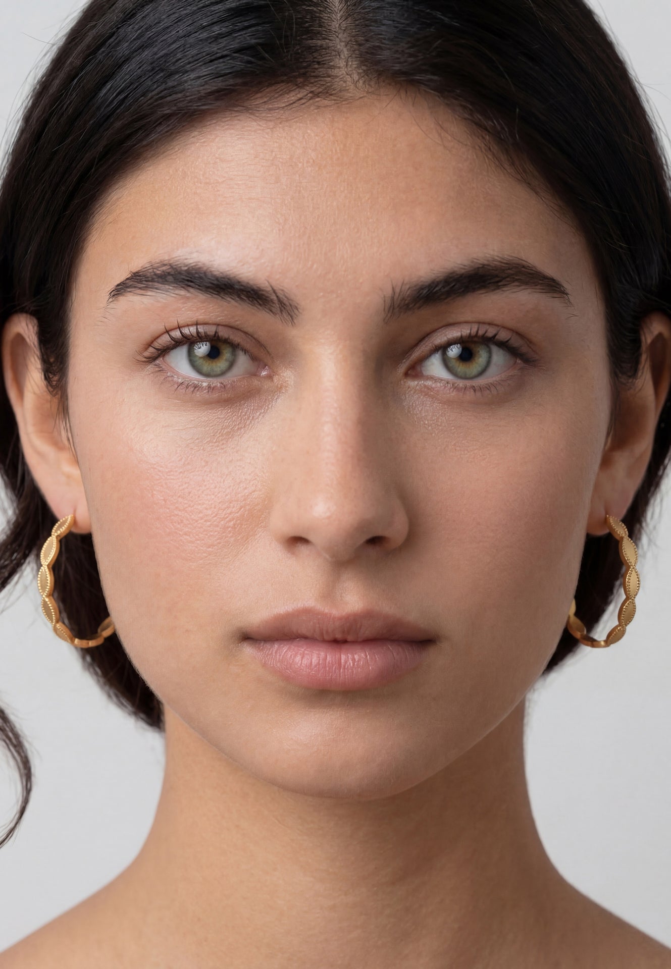 Close-up of a person wearing gold hoop earrings with a neutral background
