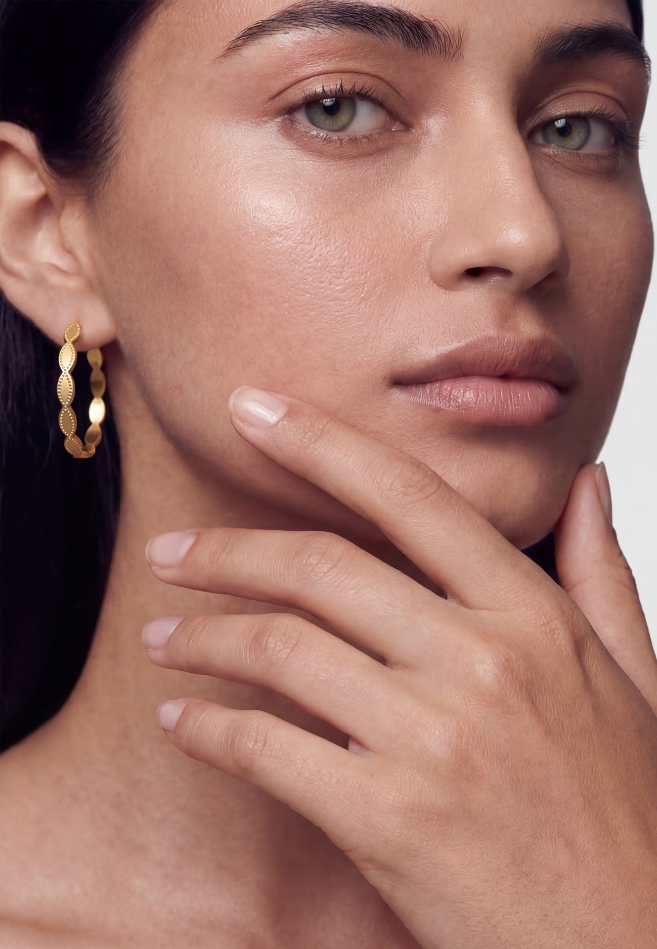 Close-up of a woman's face with gold hoop earrings and hand near her face.