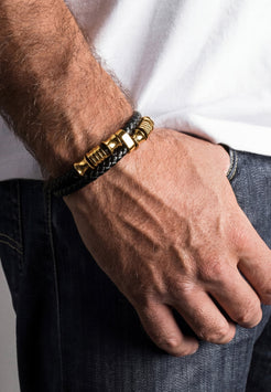 Close-up of a hand wearing a gold and black bracelet on a neutral background