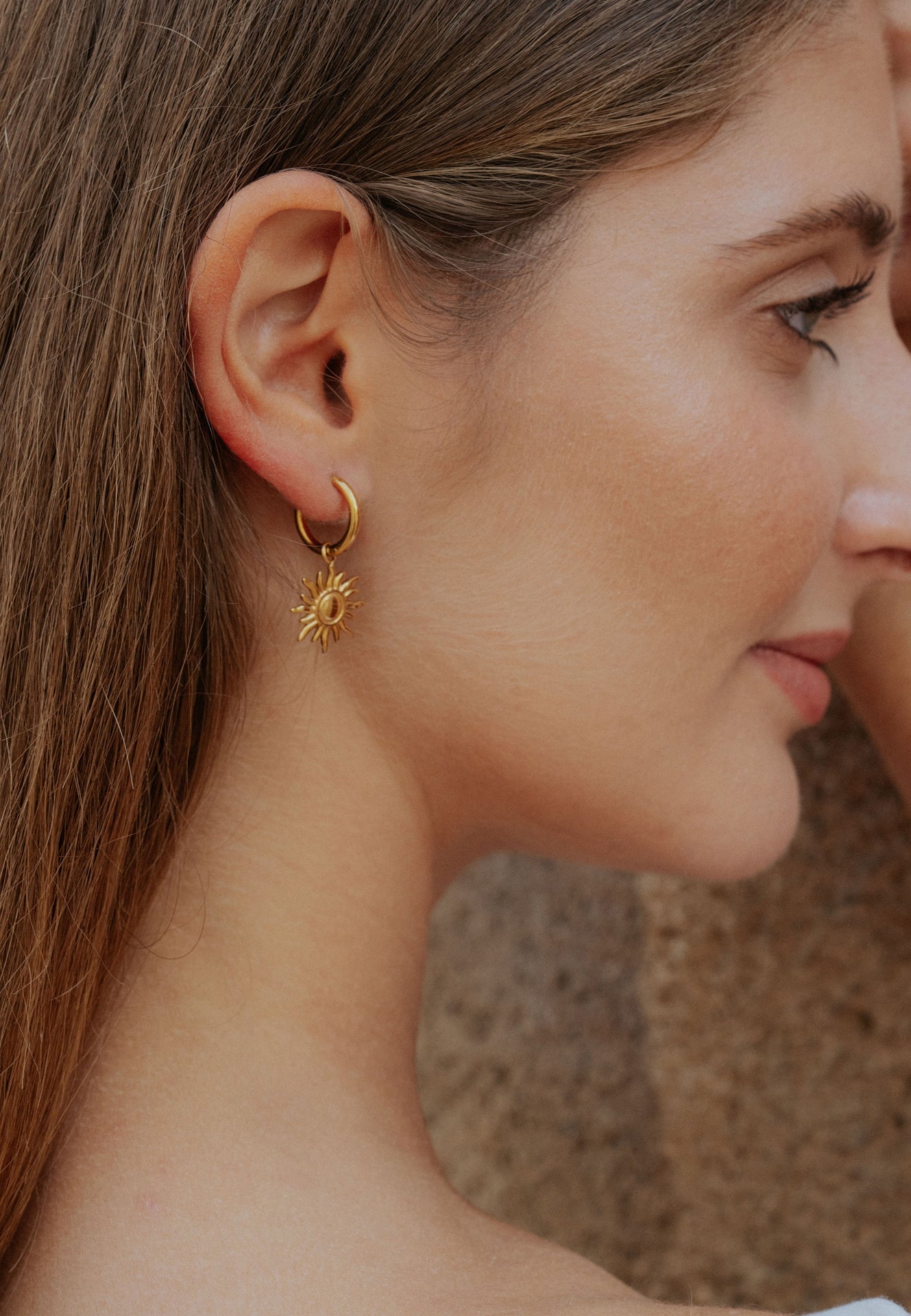 Close-up of a woman wearing a gold sun-shaped earring with a blurred background