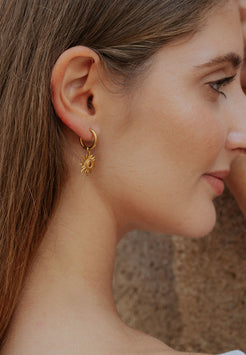 Close-up of a woman wearing a gold sun-shaped earring with a blurred background