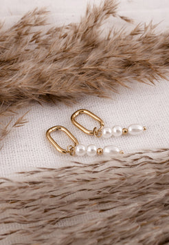 Gold earrings with pearls on a textured surface
