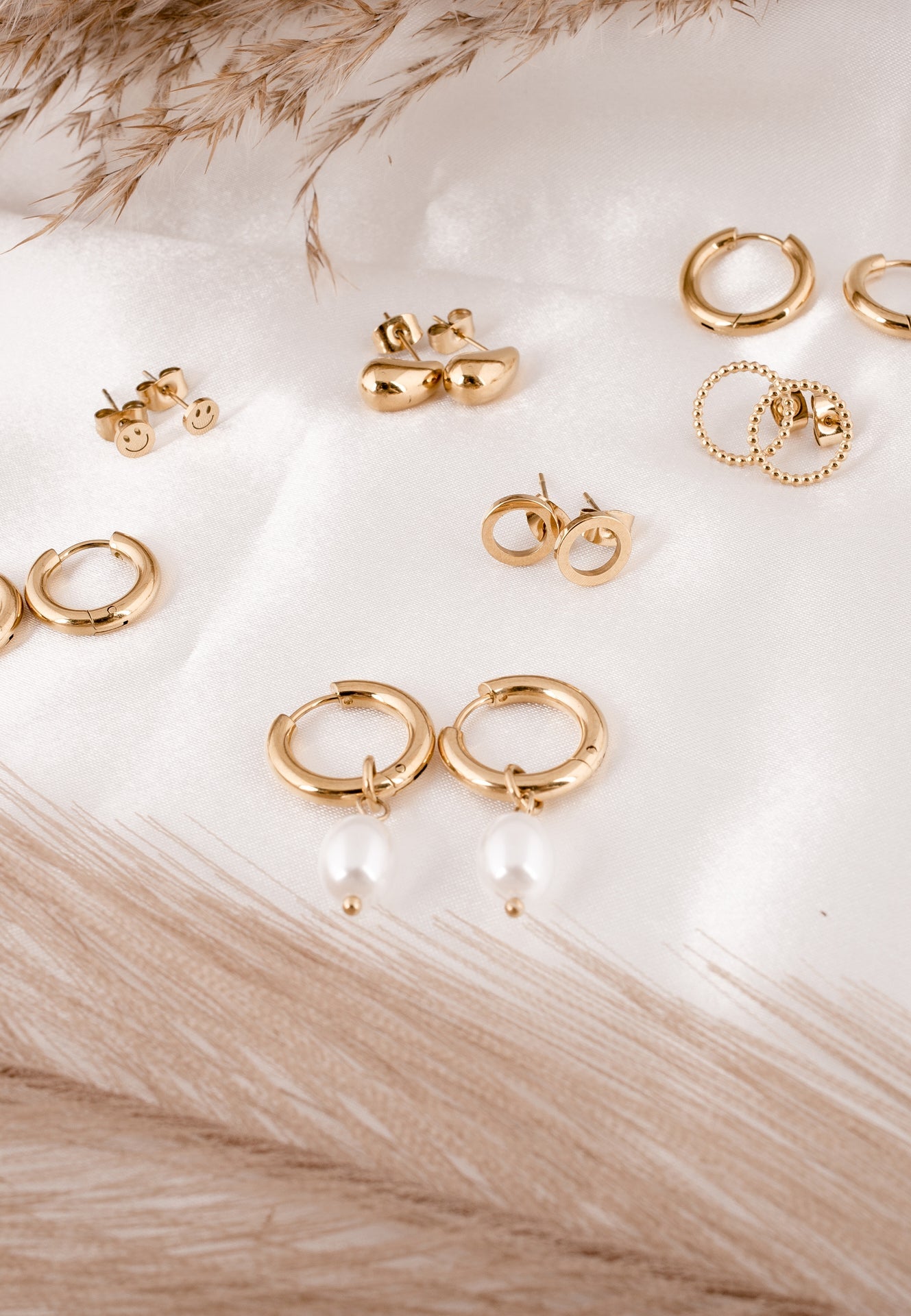 Collection of gold earrings on a light wooden surface with dried grasses.