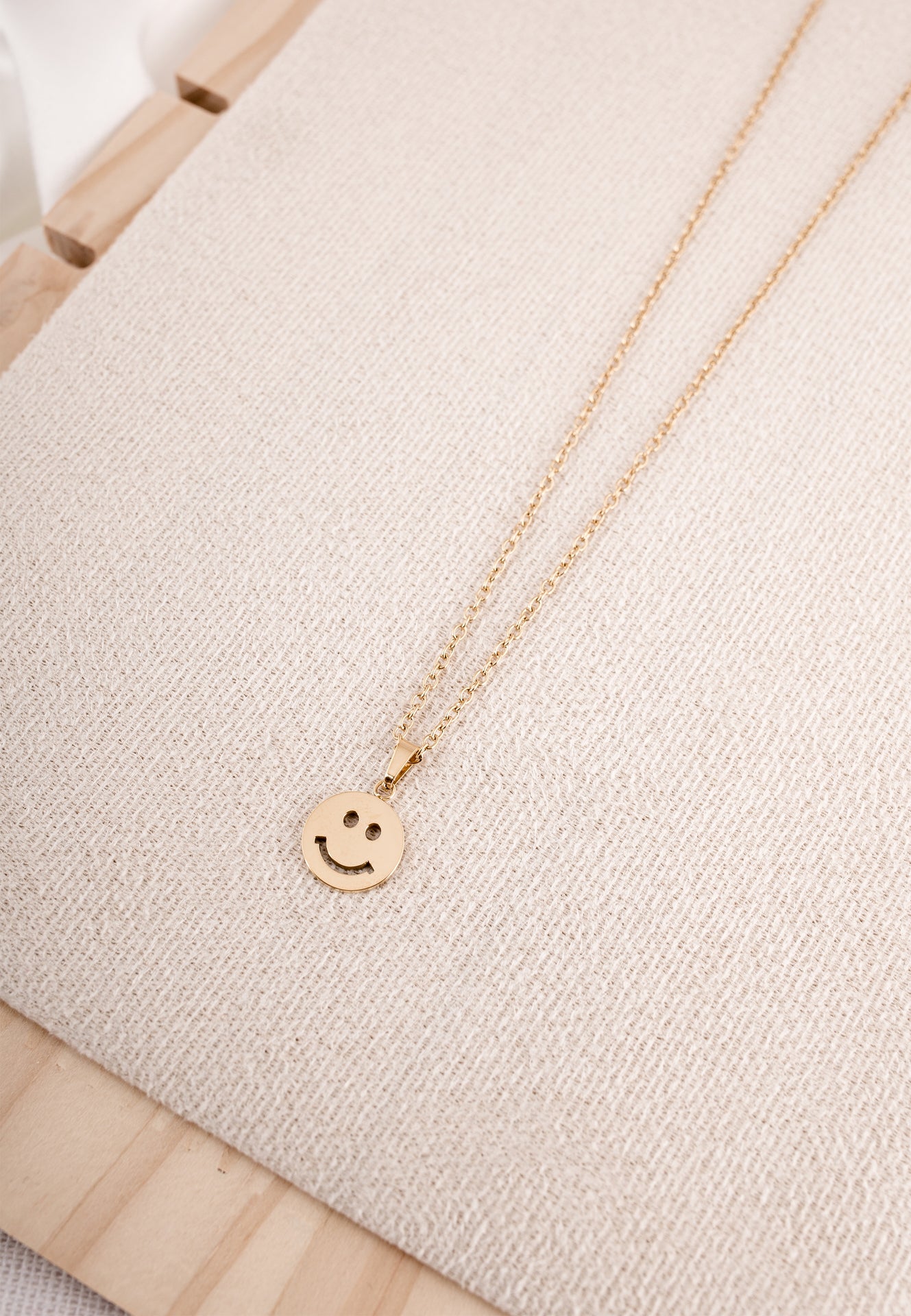 Gold necklace with a smiley face pendant on a light beige fabric background
