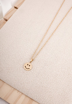 Gold necklace with a smiley face pendant on a light beige fabric background