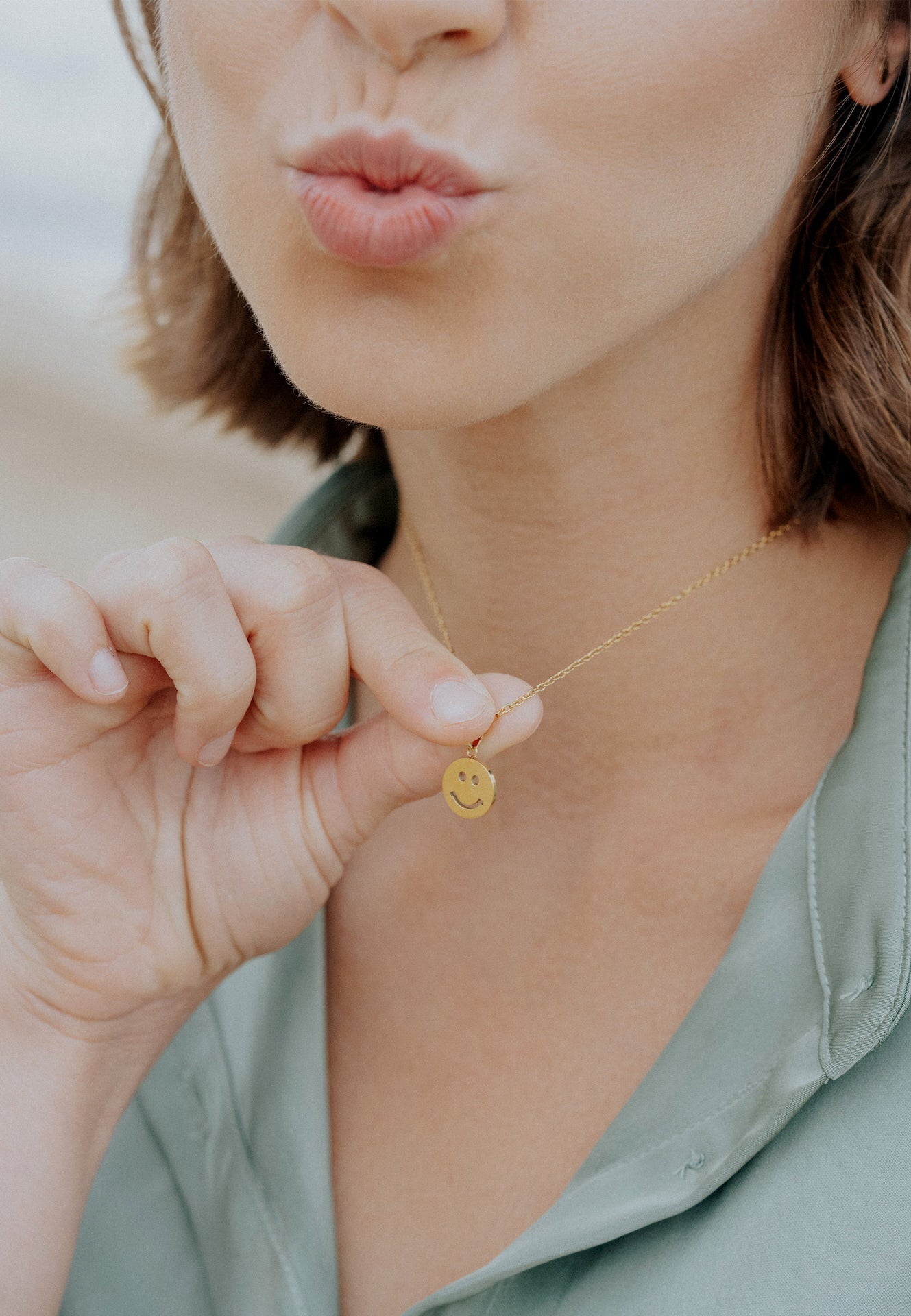 Woman holding a gold necklace with a smiley face pendant