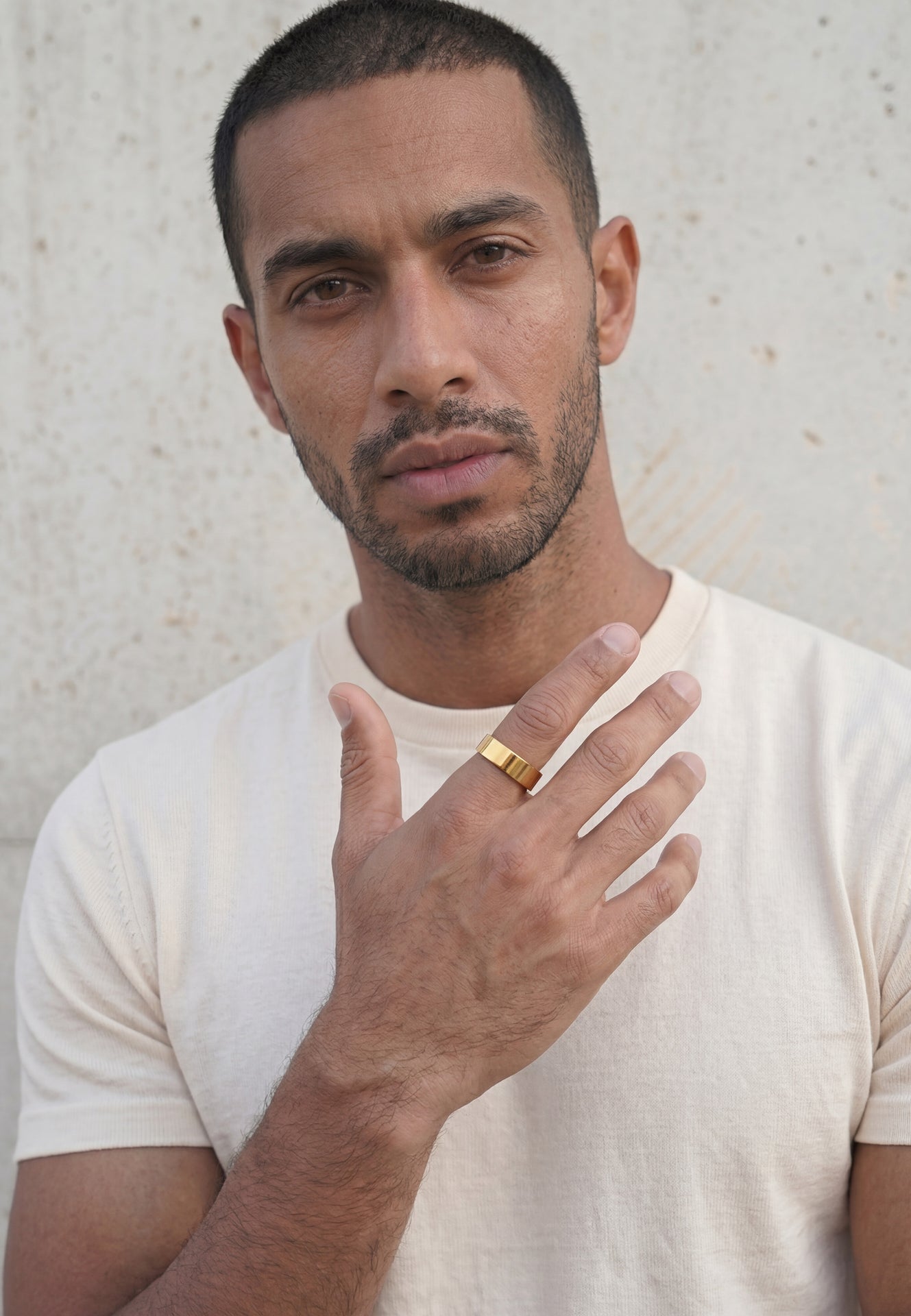 Man wearing a gold ring on his finger against a neutral background