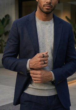 Man wearing a navy blazer over a light gray sweater with a blurred background