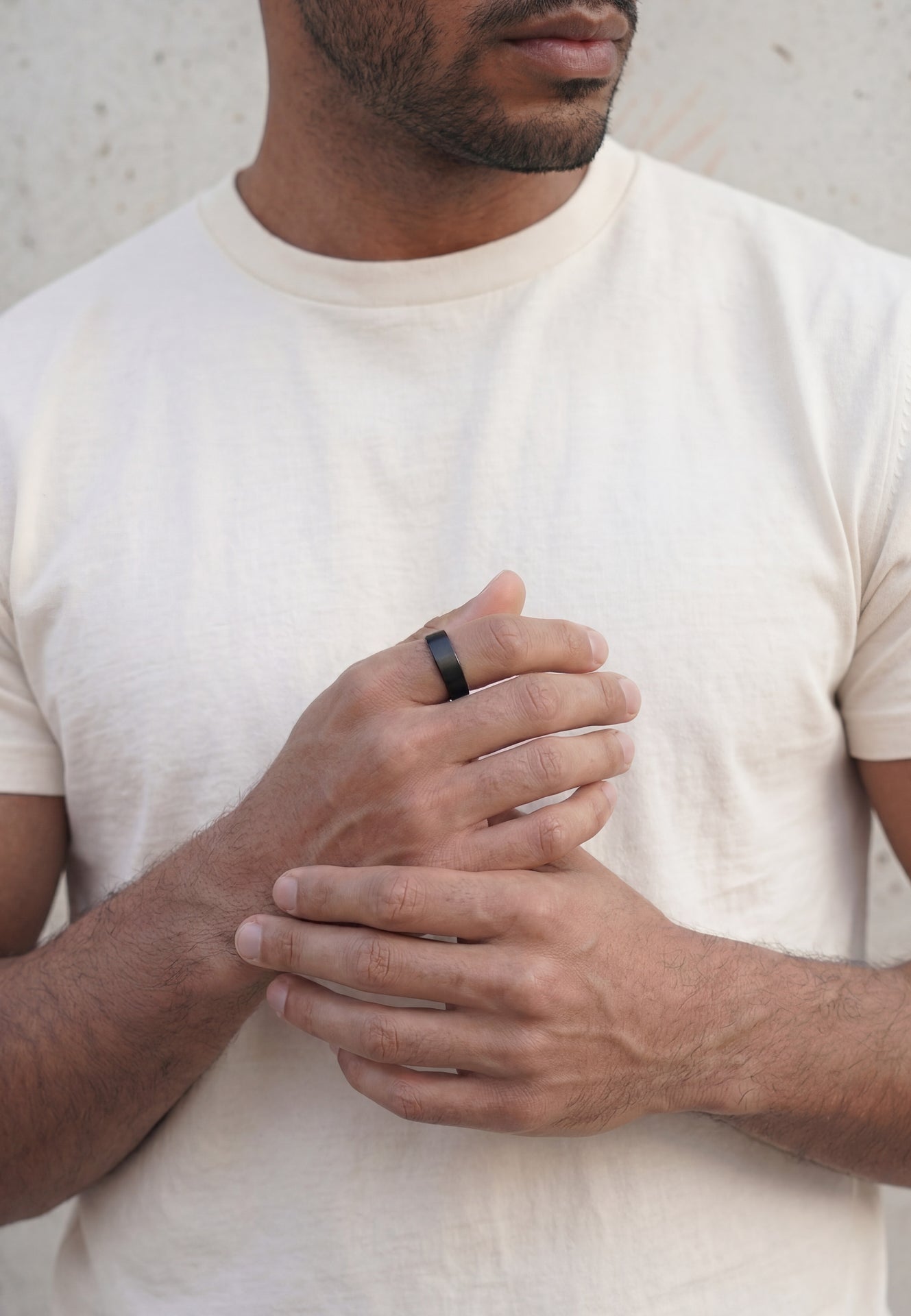 Man wearing a white t-shirt and a black ring on his finger against a neutral background