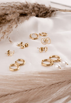 Collection of gold earrings on a light wooden surface with dried pampas grass.
