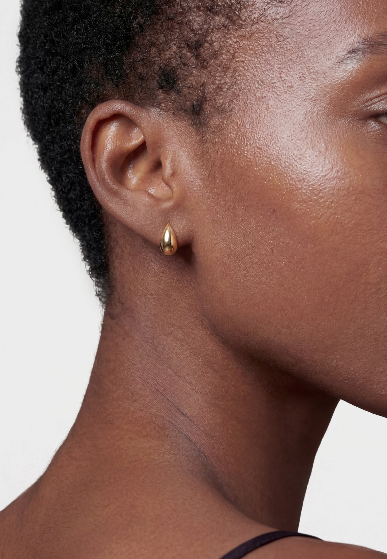Close-up of a person wearing a gold earring on a plain background