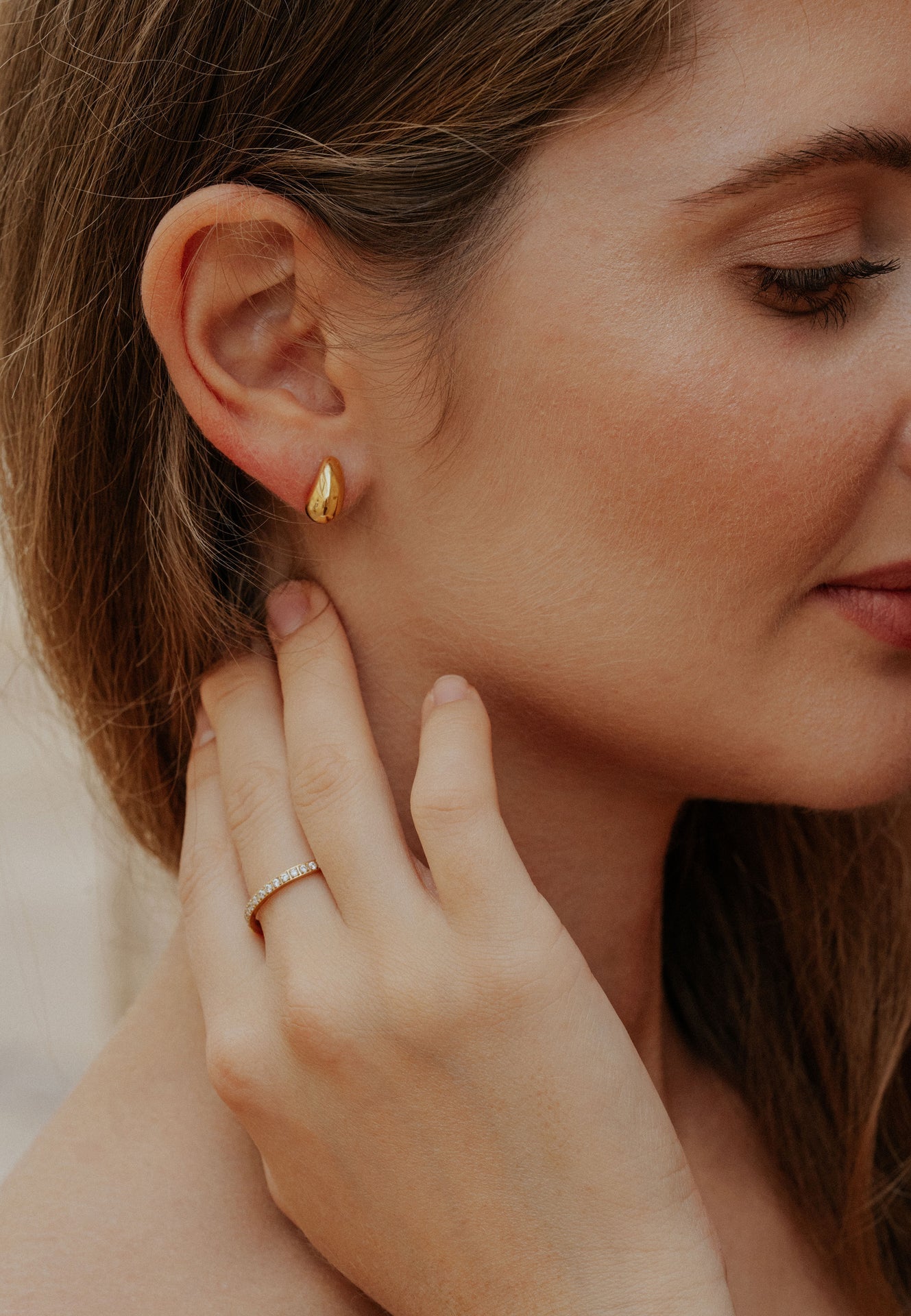 Close-up of a woman wearing a gold earring and ring, with a blurred background.