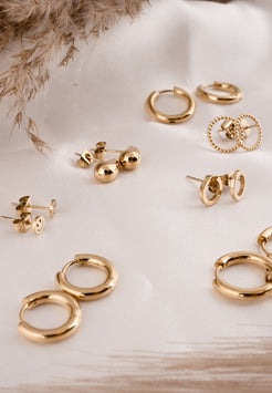 Collection of gold earrings on a light surface with dried plants.