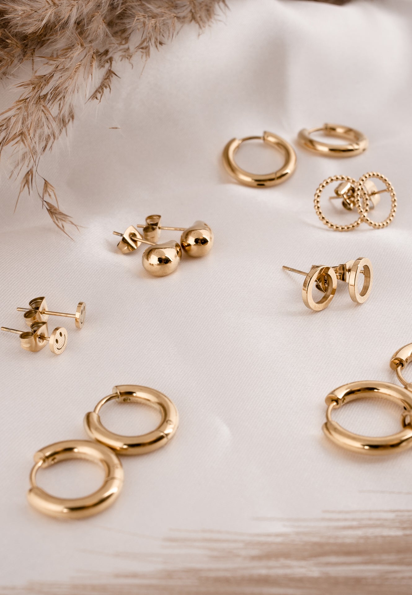 Collection of gold earrings on a light surface with dried plants.