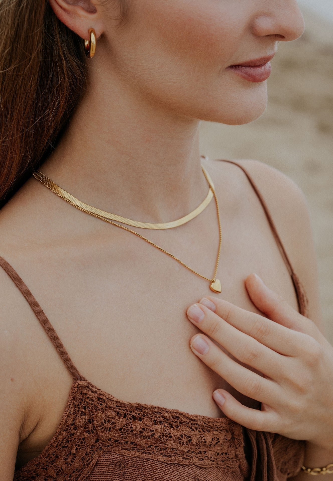 Woman wearing a gold necklace with a heart pendant, blurred background