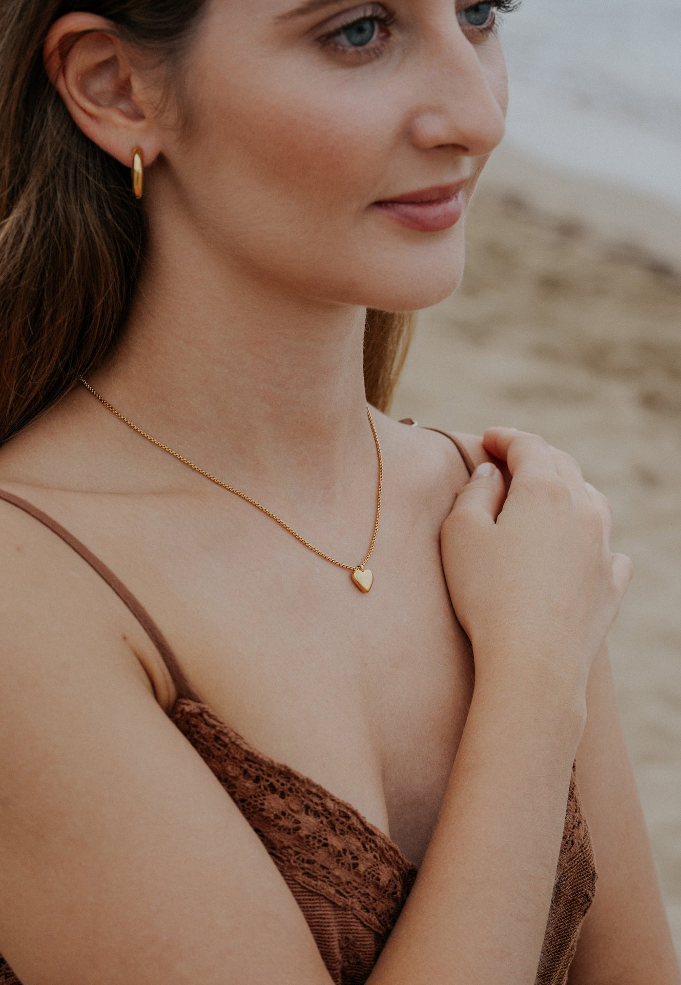 Woman wearing a gold necklace with a heart pendant on a blurred beach background
