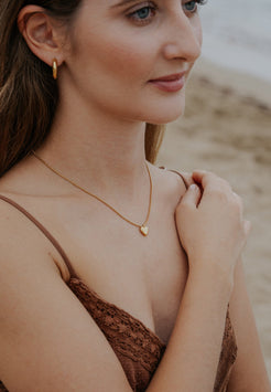 Woman wearing a gold necklace with a heart pendant on a blurred beach background