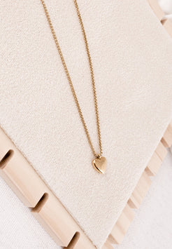 Gold necklace with a heart pendant on a textured beige surface