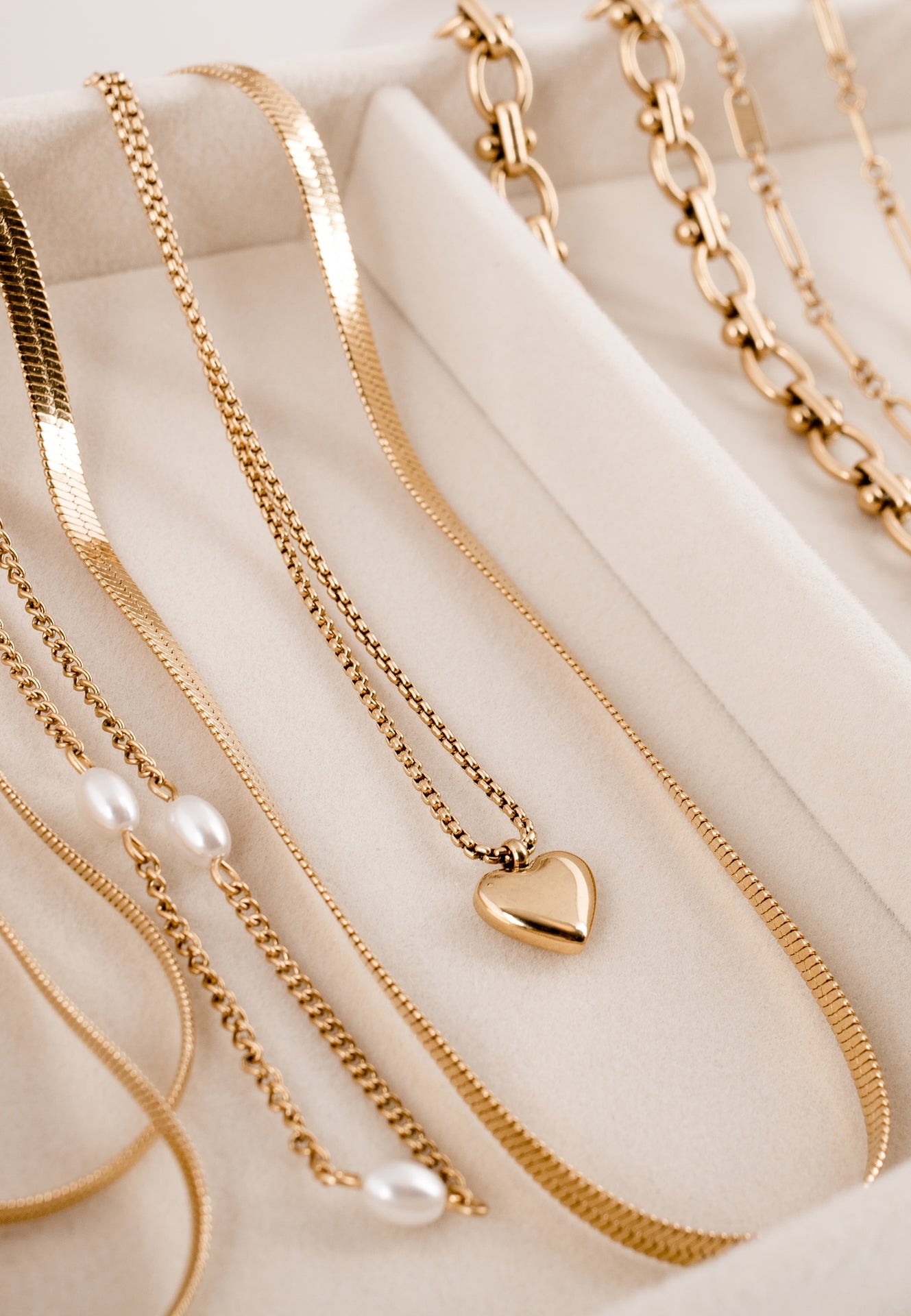 Collection of gold necklaces with heart pendants and pearls on a beige surface