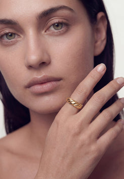 Close-up of a woman's face with a gold ring on her finger against a white background