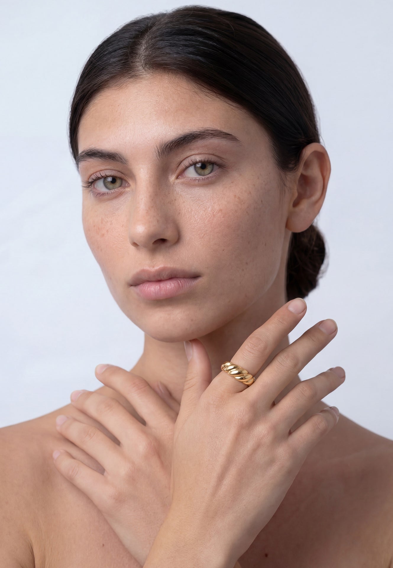 Woman wearing a gold ring on a plain background
