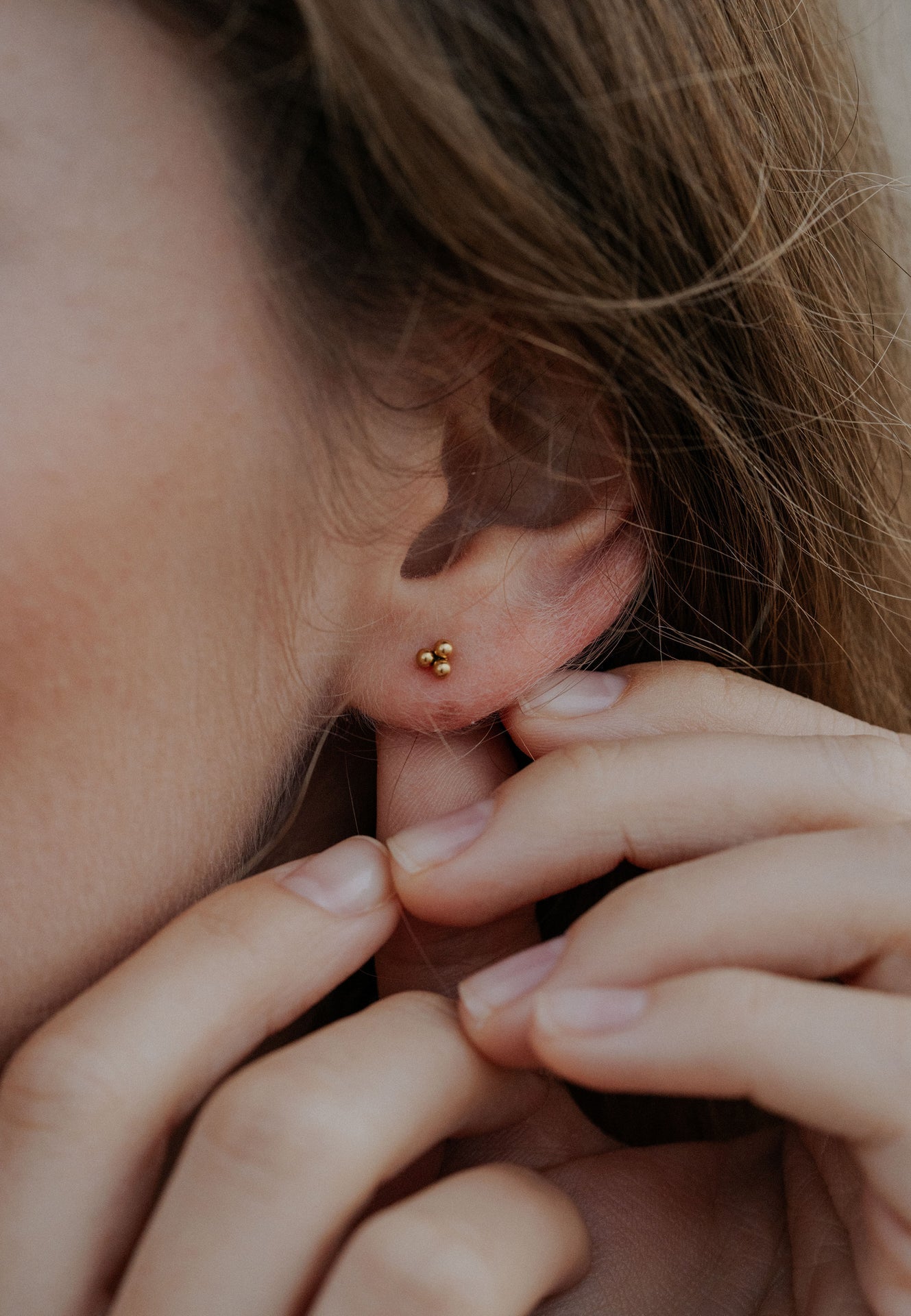 Close-up of an ear with gold stud earrings and hands touching the earlobe.
