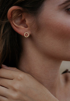 Close-up of an ear wearing a gold earring with a dark background