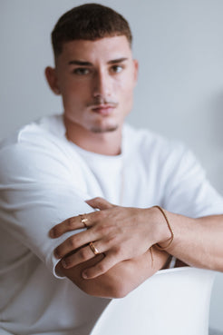 Man wearing a white shirt with gold rings and bracelets on a plain background
