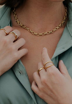 Close-up of a person wearing gold jewelry including a necklace and rings.