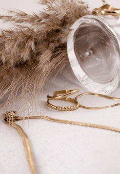 Gold jewelry including a necklace and rings on a light background with decorative elements.