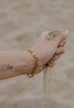 Hand with gold bracelet holding sand against a blurred natural background
