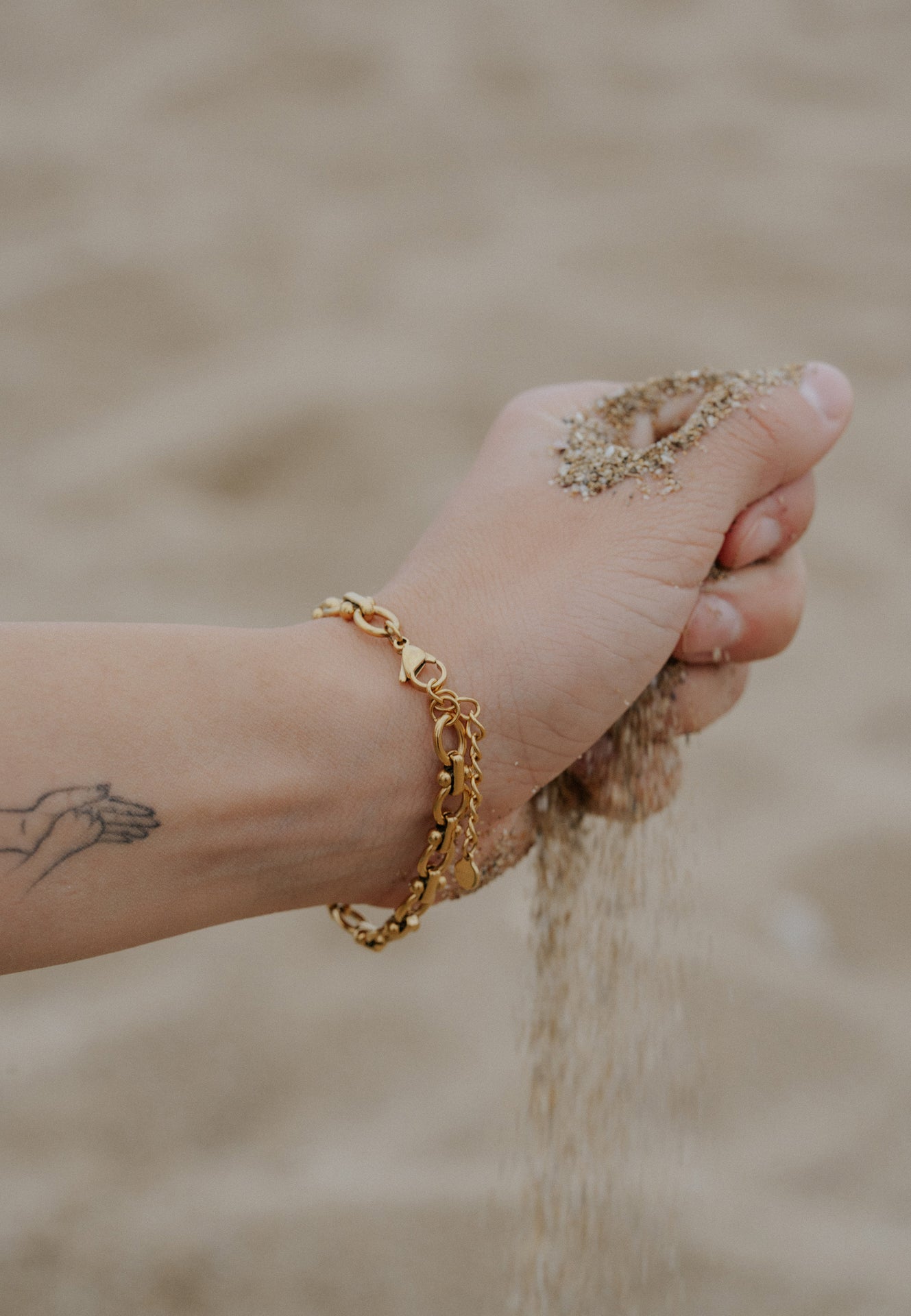 Hand with gold bracelet holding sand against a blurred natural background