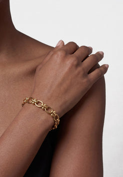 Woman wearing a black top and gold bracelet against a gray background