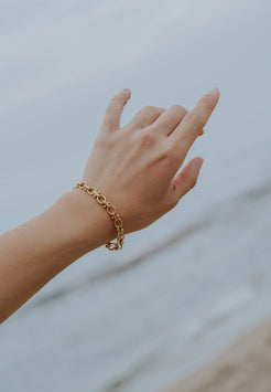 Hand wearing a gold bracelet against a blurred background
