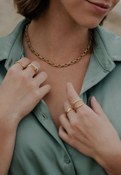 Close-up of a person wearing a gold chain necklace and rings on a blurred background