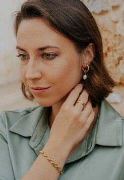 Woman adjusting an earring with a gold bracelet, wearing a light green top.