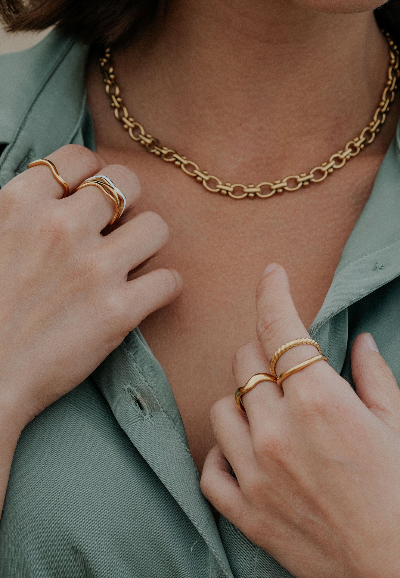Close-up of a person wearing gold jewelry including a necklace, rings, and a bracelet.