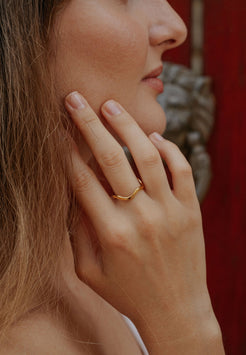 Close-up of a hand with a gold ring touching the face against a blurred background