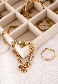 Gold jewelry including rings and a bracelet on a beige jewelry box.