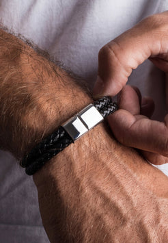 Person adjusting a black leather bracelet on their wrist against a white background
