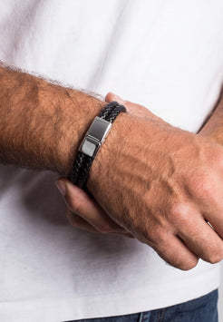 Close-up of a person wearing a black braided bracelet with a silver clasp on a white background