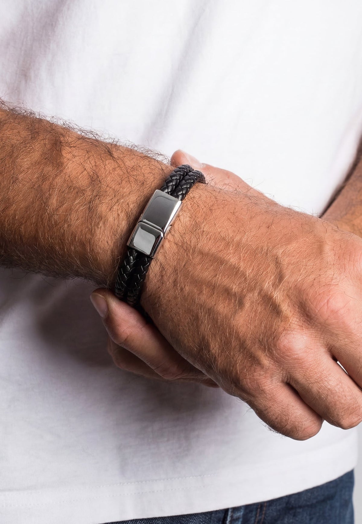 Close-up of a person wearing a black braided bracelet with a silver clasp on a white background